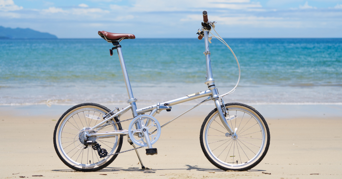 Silver folding bicycle parked on a sandy beach with blue ocean background
