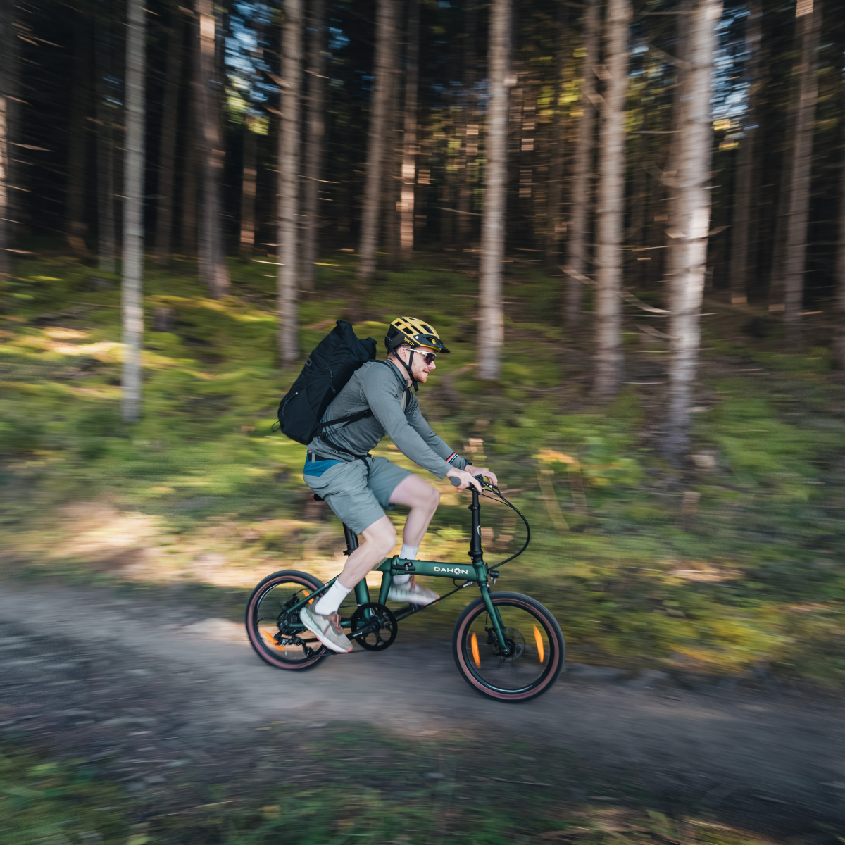 A man riding a green folding bike through a sunlit forest.