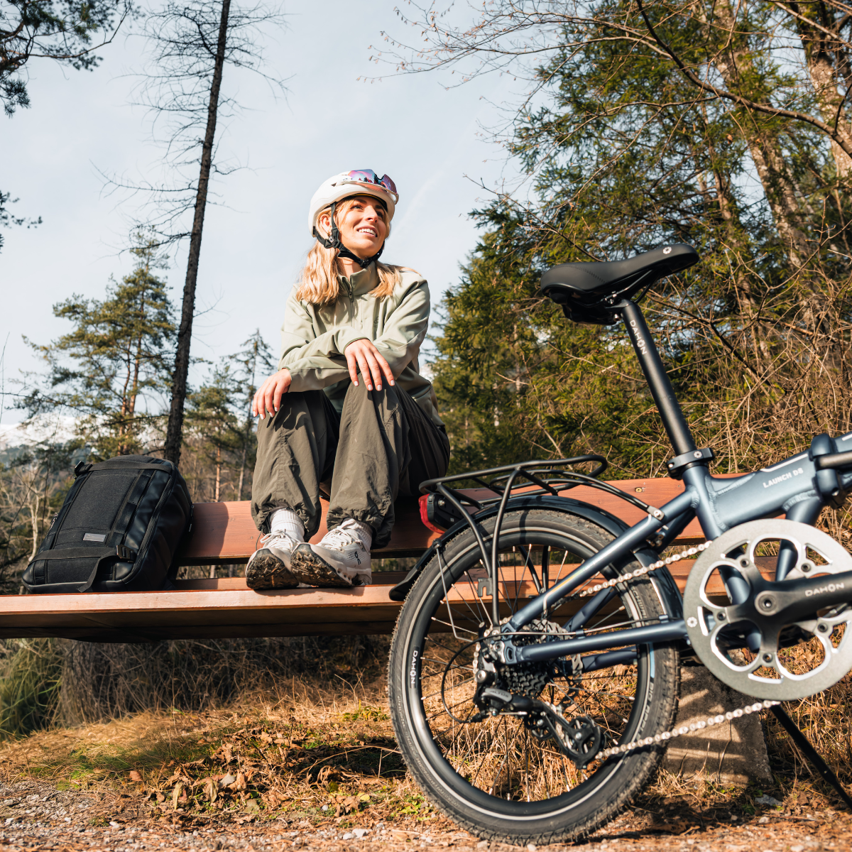 A woman in a helmet sitting on a park bench next to her bike.