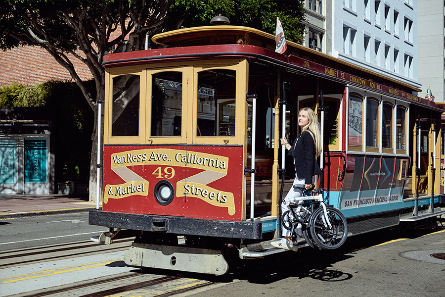 Rider holding a folded Dream D6 beside a cable car